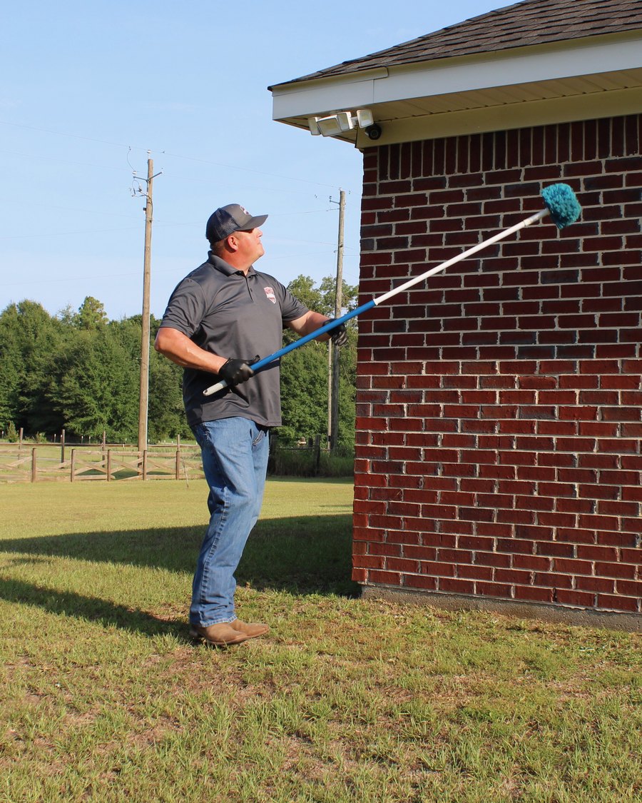 Affordable Pest Control technician brushing spider webs from the eaves of a Gulf Coast home